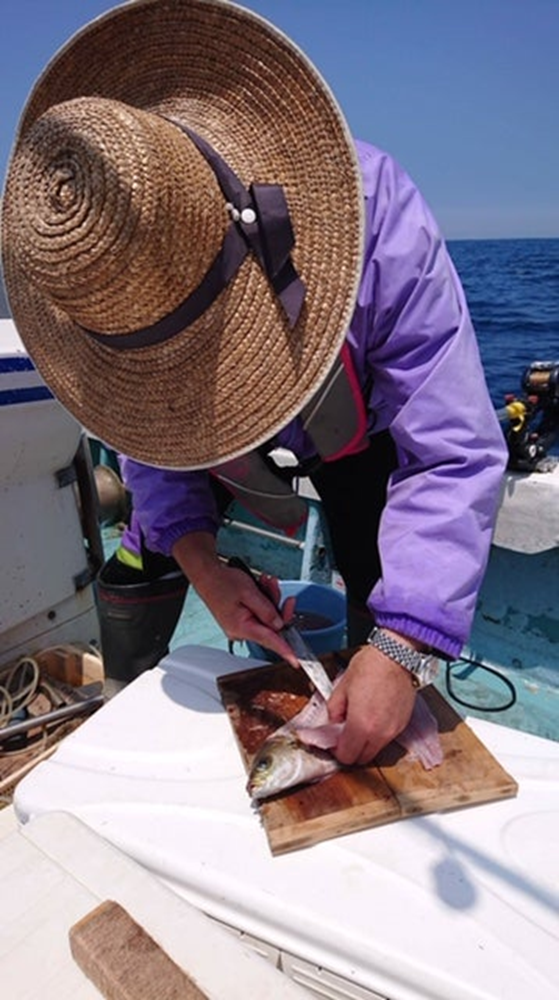 alt="釣ったイサキを船上で捌く筆者の様子"